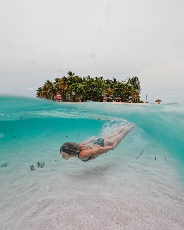 A swimmer diving underwater beside a small palm island