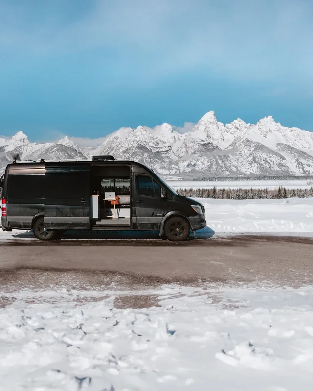 The black van parked in snow below the Tetons