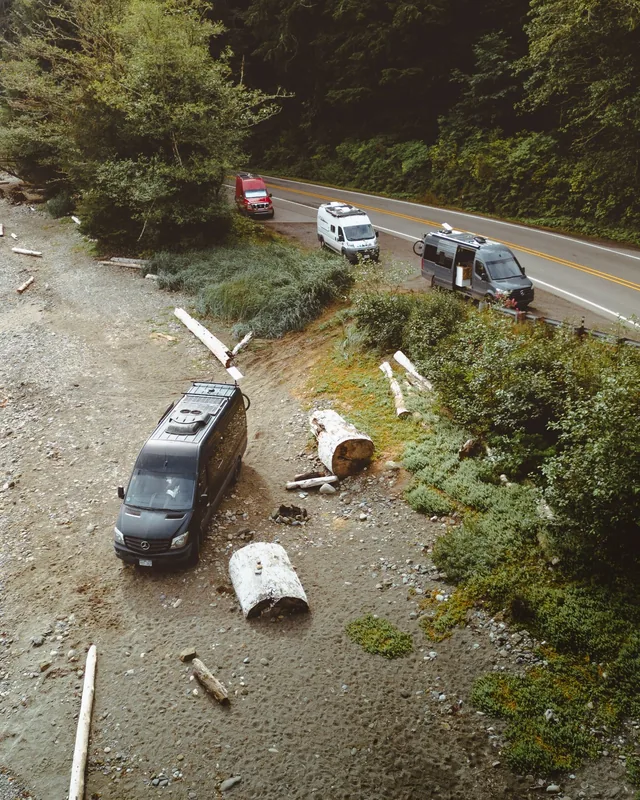 A black van parked on a beach below a forest road